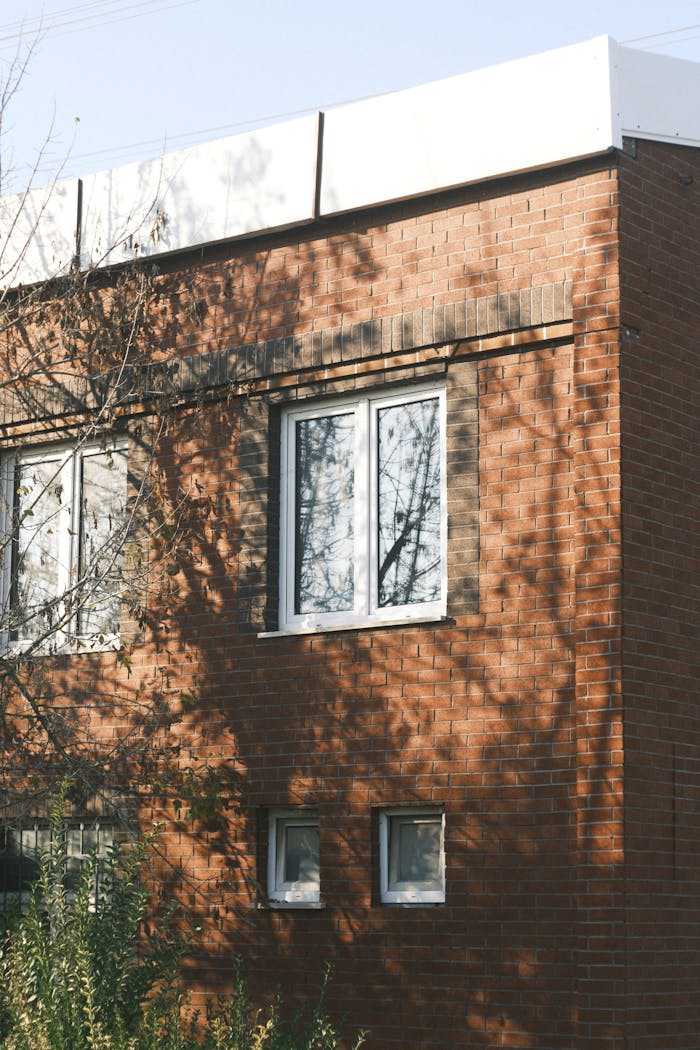 Brick building facade with tree shadows on windows, highlighting architectural details.