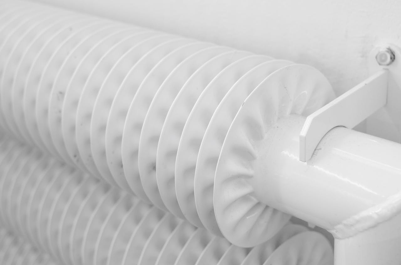 White metal tubed radiator system with pipe for industrial heating mounted to wall with hook in light room at home